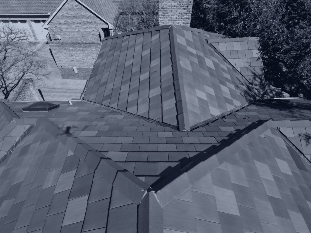 Drone photograph looking down on a slate roof where four slopes meet, the hips and valleys measured plane by plane during an inspection — the kind of roof documented on property damage claims in Arlington.